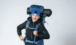 Un jeune homme souriant avec un grand sac à dos bleu, prêt pour l'aventure. On se demande : sac 70 litres combien de kilos ?