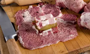 Przygotowanie zrazów z karkówki: rozbite plastry mięsa z boczkiem, ogórkiem i cebulą, obok przyprawy i nóż.