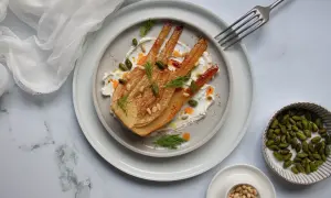 Un plat de fenouil au four, doré et tendre, servi sur une crème onctueuse, garni de pistaches, pignons et d'aneth frais.