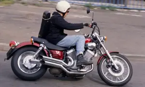 Mężczyzna w kasku jedzie na czerwonym motocyklu Yamaha Virago, z futerałem na instrument muzyczny przypiętym z tyłu.