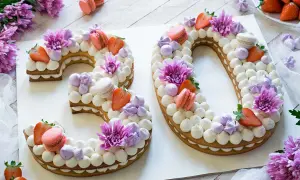 Una torta numero 30 decorata con panna, fragole, macarons e fiori viola.