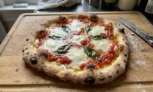 En perfekt napolitansk pizza med bubblig kant, smält mozzarella och färsk basilika på en träskärbräda.