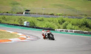Motocyklista w czerwonym kombinezonie pochylony na zakręcie toru wyścigowego.