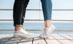 Para na drewnianym pomoście, w białych trampkach i jeansach. Idealne converse stylizacje damskie na letni dzień nad morzem.