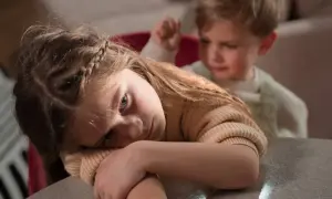 Smutna dziewczynka z warkoczem opiera głowę na rękach. Czy dziecko pamięta traumę? Za nią widać zamazanego chłopca.