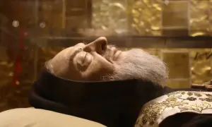 Szklana trumna z ciałem Ojca Pio, z widoczną twarzą, brodą i ozdobnym szalem.