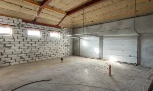 Intérieur d'un garage en construction, prêt à isoler. Murs en parpaings, plafond isolée, portes de garage sectionnelles blanches.