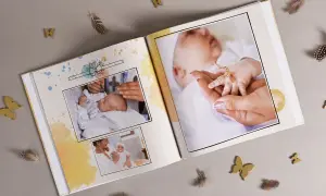Otwarta księga pamiątkowa z fotografiami niemowlęcia, ozdobiona piórkami i motylkami.