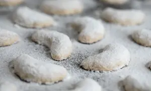 Zarte Vanillekipferl, mit Puderzucker bestäubt, liegen auf einem Blech. Ein süßer Duft liegt in der Luft.