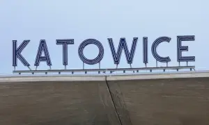 Napis KATOWICE z niebieskimi neonami na tle błękitnego nieba.