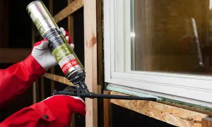Persona con guantes rojos aplica espuma de poliuretano no expansiva alrededor de una ventana.