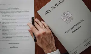 Akt notarialny z pieczęcią Kancelarii Notarialnej Tomasza Kłysa. Widoczny wzór dokumentu i dłoń z długopisem.