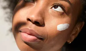 Geste doux pour mettre de la crème sur la joue d'une jeune femme, illuminée par la lumière du soleil.