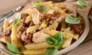 Penne z kurczakiem i suszonymi pomidorami, udekorowane świeżą bazylią. Pyszne danie na obiad.