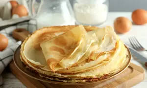 Pila di crepes dorate, pronte per essere farcite. Ingredienti per una ricetta crepes dolci perfetta: uova, latte e farina sullo sfondo.