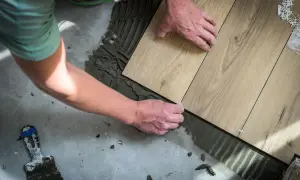 Man placing wood-look tiles on cement floor. Learn como colocar el parquet horizontal o vertical para un acabado perfecto.