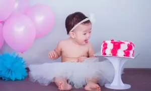 Słodki roczek! Dziecko w tiulowej spódniczce z zaciekawieniem patrzy na tort. Różowe balony dodają uroku.