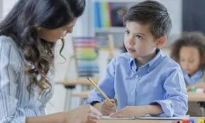 Nauczycielka wspiera chłopca w szkole podstawowej dla dzieci z zespołem Aspergera. Uczą się razem przy biurku.