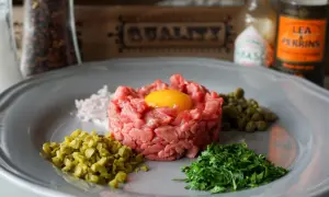 Un plat de tartare de boeuf frais, garni d'un jaune d'oeuf, avec des câpres, des cornichons hachés, des échalotes et du persil.