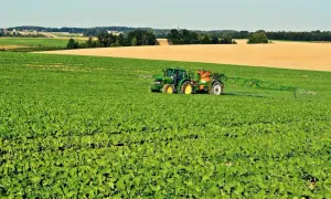 Zielony traktor z opryskiwaczem na polu rzepaku. W tle pola i wieś. Jakby uderzenie **inazuma** w krajobraz.