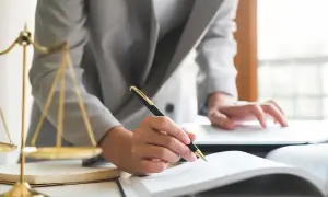 Prawnik sporządza testament, który reguluje spadek po mężu bez dzieci. Obok waga sprawiedliwości.