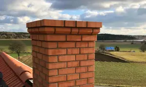 Nyrenoverad tegelstenstopp på en skorsten med vacker landsbygd i bakgrunden. Undrar du över renovera skorsten pris?