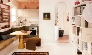 Acogedora casa pequena con cocina verde, sofá cama, mesa amarilla y estanterías llenas de objetos.
