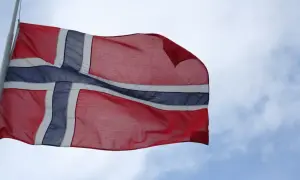 Flaga Norwegii powiewa na wietrze na tle błękitnego nieba z chmurami.