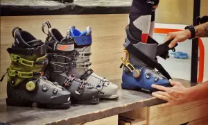 Różne buty narciarskie, w tym zielone K2 i szare Salomon. Dłoń dopasowuje niebieski but, pokazując, co to jest Mondopoint – standard rozmiarów butów narciarskich.