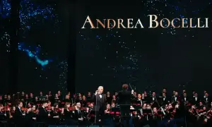 Andrea Bocelli koncert 2026. Wokalista śpiewa z orkiestrą symfoniczną na tle gwieździstego nieba.