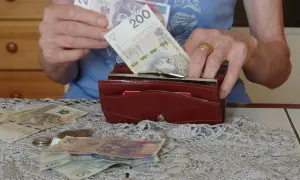 Dłonie wkładają banknot 200 zł do portfela. Na stole leżą inne banknoty i monety, co skłania do refleksji, ile wynosi średnia emerytura.