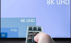 Dłoń trzymająca pilot do telewizora, na ekranie w **hd format** widać porównanie rozdzielczości: 8K UHD, 4K UHD, FHD i SD.