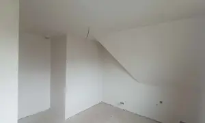 Wnętrze pokoju ze skośnym sufitem, ściany pokryte tynkiem gipsowym bez gładzi, gotowe do malowania.