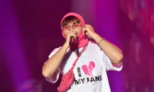 Mata raper w różowej kominiarce i okularach, z torbą na ramię i koszulką "I MY FANS", śpiewa na koncercie.