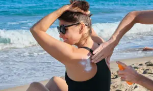 Kobieta na plaży smaruje plecy kremem z filtrem. Zastanawiasz się, ile trzeba byc na słońcu, żeby się opalić? Pamiętaj o ochronie!