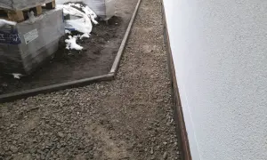 Ścieżka z tłucznia drogowego obok białej ściany budynku i palet z materiałami budowlanymi.