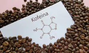 Ziarna kawy otaczają kartkę z napisem "Kofeina" i jej wzorem chemicznym. Czy kofeina w tabletkach jest zdrowa?