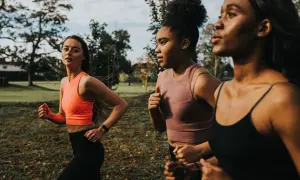 Tre donne con fisico da corsa si allenano all'aperto, immerse nel verde di un parco.
