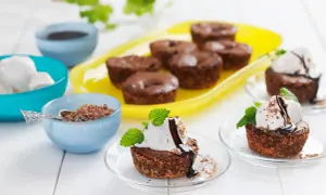 Kladdkakemuffins recept: Mörka, saftiga kladdkakemuffins med kokos, toppade med vaniljglass, chokladsås och mynta. Serveras med chokladströssel.