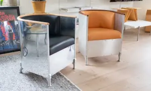 Två fåtöljer i källemo aluminium med svarta och orange lädersitsar. En spegelblank yta reflekterar rummet.