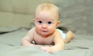 Bebé boca abajo, con los brazos apoyados, mostrando el reflejo de enderezamiento en su mirada curiosa.