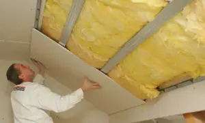 Pracownik montuje płyty gipsowo-kartonowe na poddaszu, nad wełną mineralną. Pokazuje, jak kłaść wełnę na poddaszu.