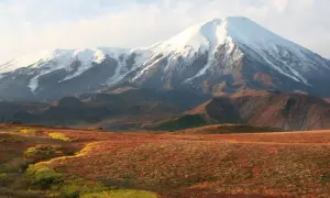 Majestätischer schneebedeckter Vulkan in einer weiten russischen Landschaft mit herbstlich gefärbten Hügeln im Vordergrund.