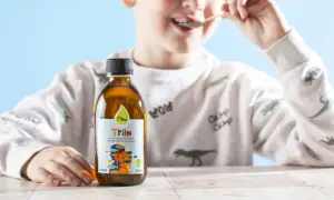 Chłopiec je tran z łyżeczki. Obok stoi butelka z płynnym tranem.