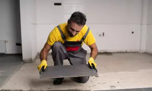 Obrero con guantes amarillos prepara un azulejo gris para pegar con Sikaflex en una obra.
