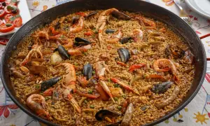 Une paella valenciana généreuse, débordant de riz, crevettes, moules et langoustines, prête à être dégustée.