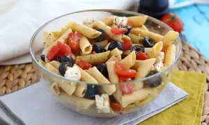 En skål med läcker pasta sallad med penne, svarta oliver, tomater och fetaost. Perfekt för en lätt lunch.