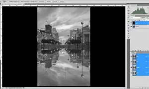Interface Photoshop : une image de ville en noir et blanc avec ses reflets dans l'eau. Le calque "Layer 1" est sélectionné, prêt à mettre un calque en noir et blanc.