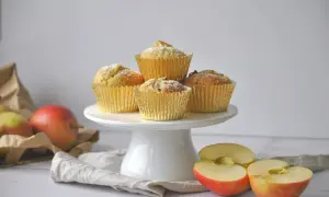 Goldene Muffins mit Puderzucker, daneben Äpfel und eine Tüte. Ein leckeres apfelmuffins rezept zum Nachbacken.