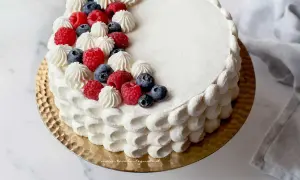Torta rotonda compleanno decorata con panna, lamponi e mirtilli. Un dolce perfetto per ogni festa.